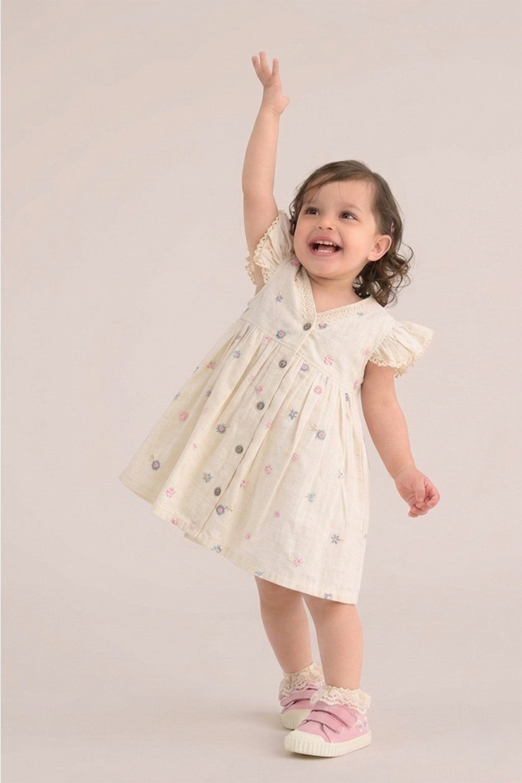 Child wearing a white dress with short sleeves on a plain background