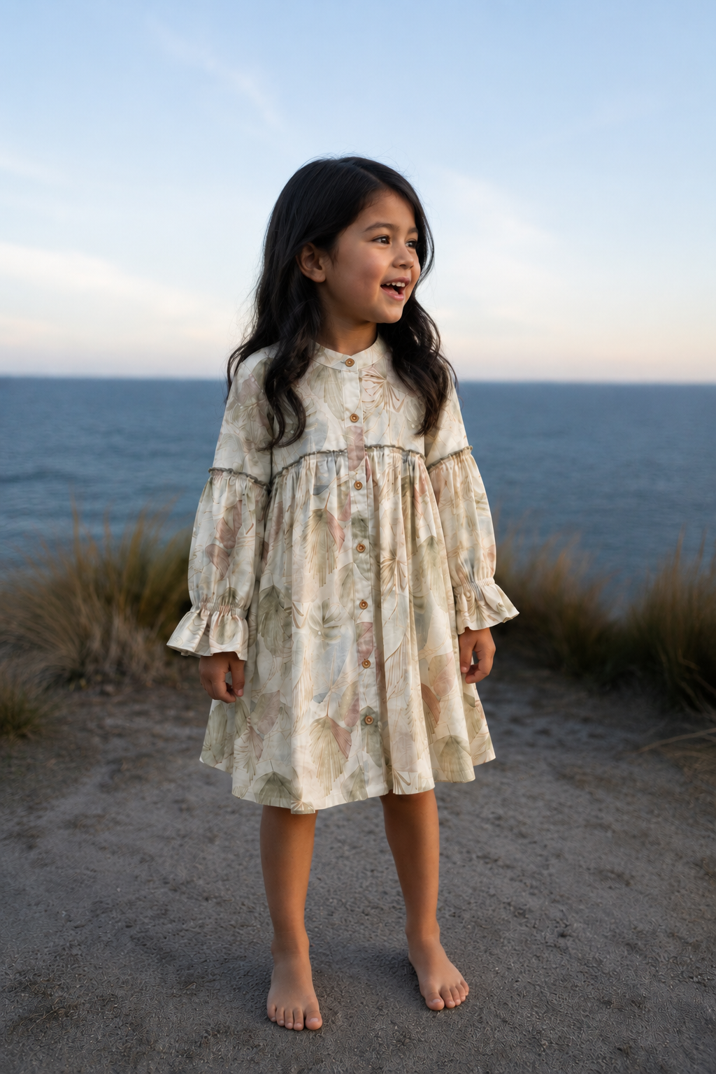 Young girl in a floral dress standing on a beach with ocean in the background